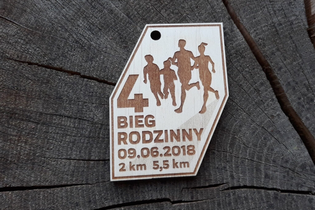 Pamiątkowy medal z drewna o naturalnym wykończeniu, przedstawiający biegnących sportowców i napis 4 Bieg Rodzinny, oraz datę.