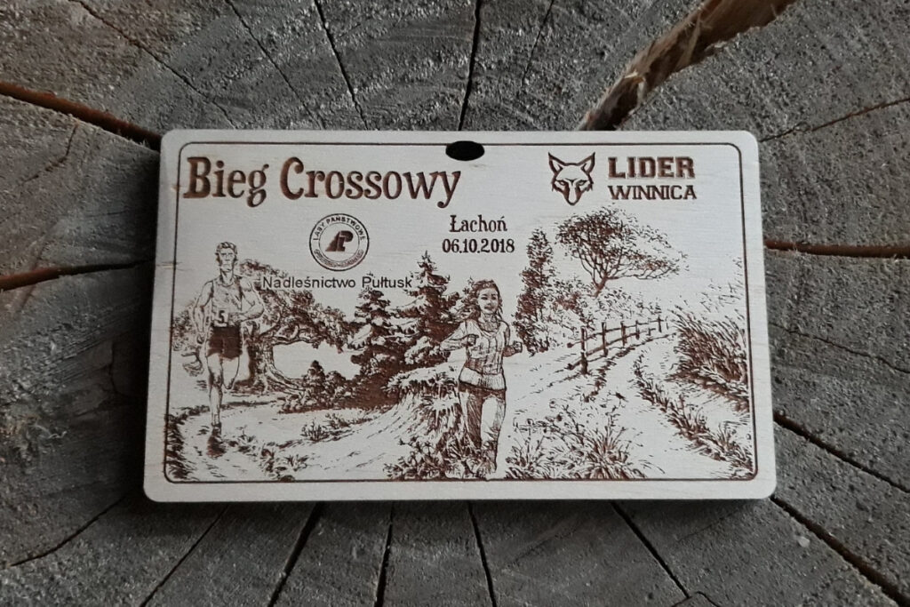 Drewniany medal na bieg crossowy z grawerem dynamicznych sylwetek biegaczy w terenie.