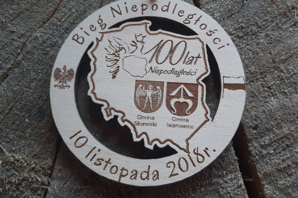 Drewniany medal na Bieg Niepodległości z herbami gmin Słomniki i Iwanowice oraz ażurowym konturem Polski.