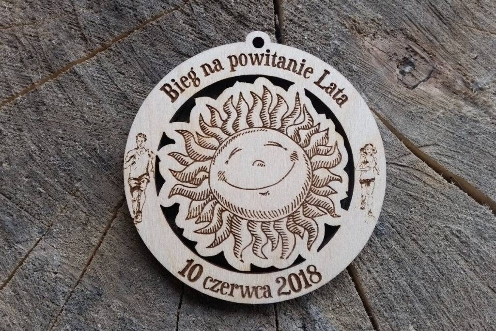 Drewniany medal na Bieg na Powitanie Lata 2018 z ażurowo wyciętym słońcem w centrum.