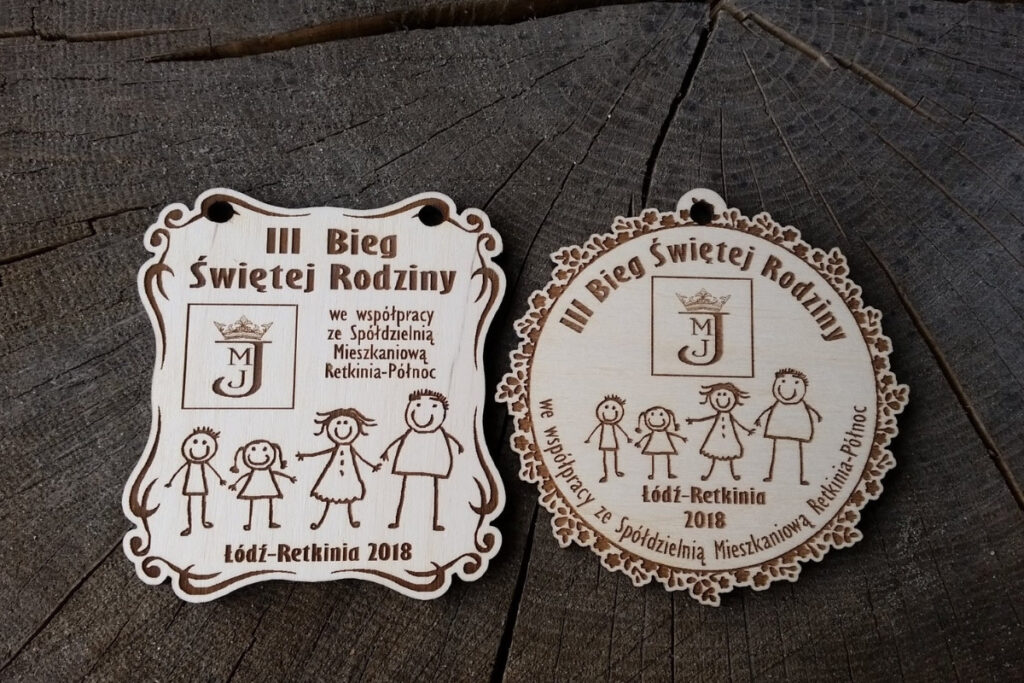 Projekty drewnianych medali na III Bieg Świętej Rodziny z grawerowaną sylwetką rodziny i detalami, zawieszony na ekologicznym sznurku.