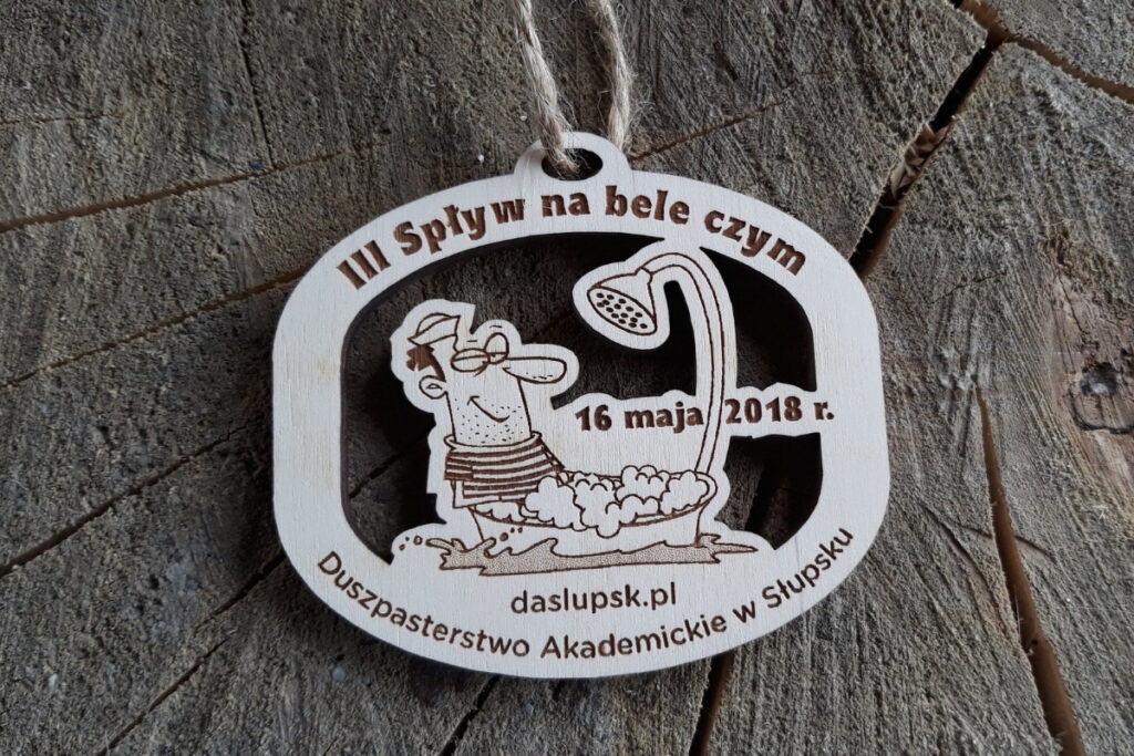 Drewniany, ażurowy medal na III Spływ na Bele Czym z wyciętym motywem śmiesznej postaci w bańce pod prysznicem.