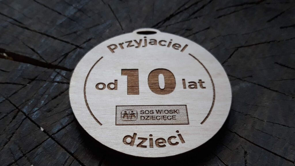Drewniany medal pamiątkowy z napisem „Przyjaciel Dzieci”, ozdobiony grawerem o logotypem SOS Wioski Dziecięce.