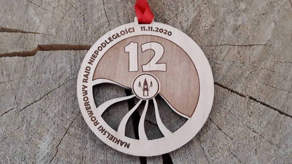 Okrągły drewniany medal na Rowerowy Rajd Niepodległości, ozdobiony ażurem imitującym szprychy rowerowe.