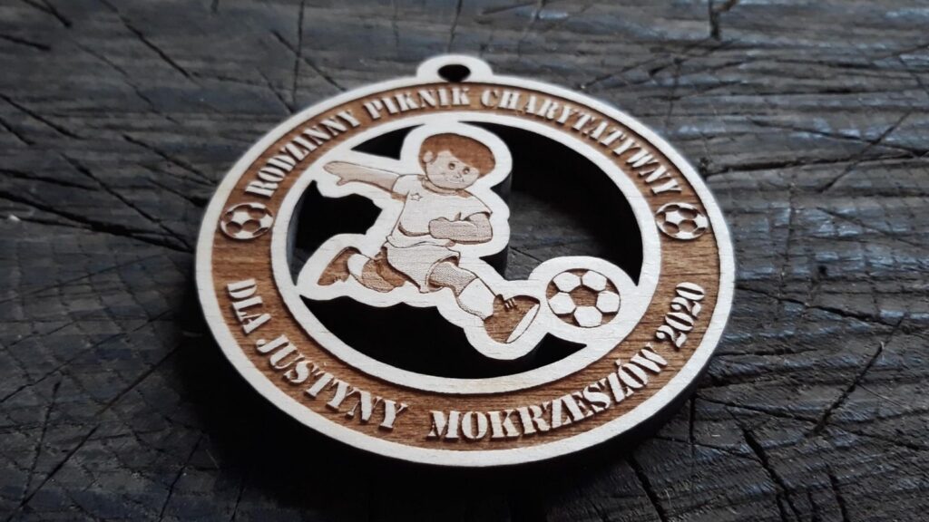 Ażurowy drewniany medal charytatywny z wyciętą sylwetką piłkarza, przygotowany na Rodzinny Piknik Charytatywny dla Justyny w Mokrzeszowie.
