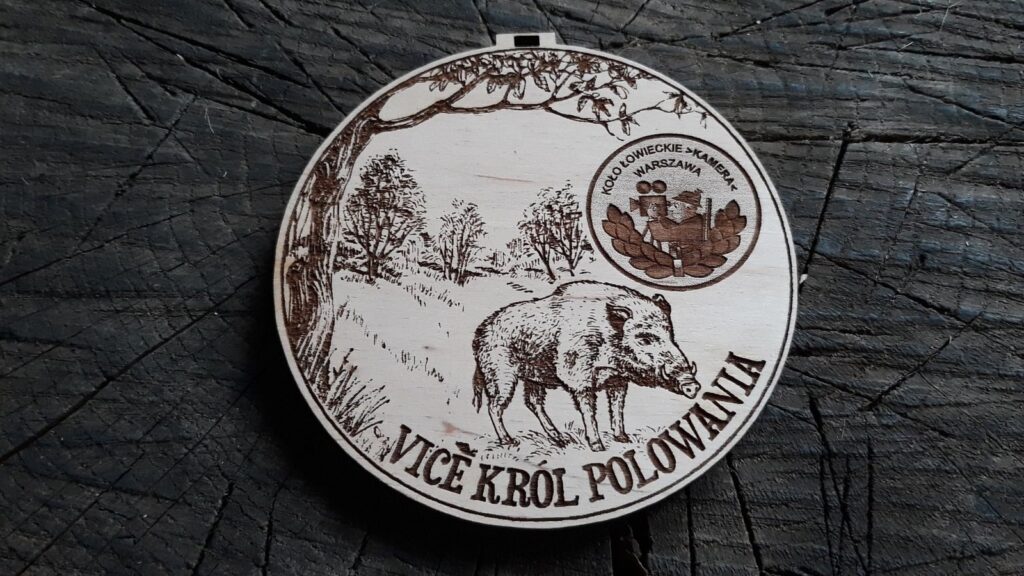 Okrągły medal myśliwski z drewna z grawerem dzika i napisem „Król Polowania”, personalizowany logiem koła łowieckiego.