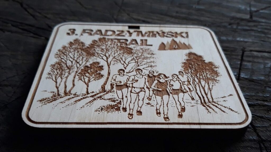 Prostokątny drewniany medal na bieg leśny z wygrawerowanymi sylwetkami biegaczy na tle lasu i detalami.