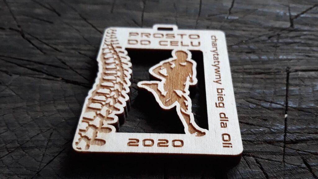 Ażurowy drewniany medal charytatywny z wyciętym symbolem kręgosłupa i sylwetką biegacza, przygotowany na bieg wspierający leczenie.
