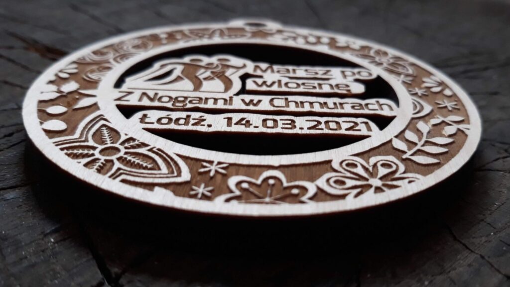Ażurowy drewniany medal na „Marsz po Wiosnę” z precyzyjnie wyciętymi sylwetkami osób uprawiających Nordic Walking wewnątrz ozdobnej ramki z grawerem.