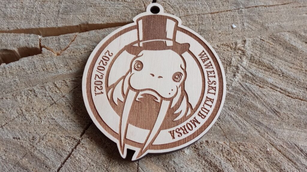 Okrągły drewniany medal dla klubu morsów z humorystycznym grawerem przedstawiającym morsa w eleganckim kapeluszu.