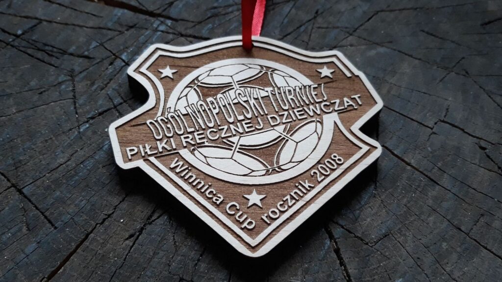 Drewniany medal sportowy na Ogólnopolski Turniej Piłki Ręcznej Dziewcząt, z grawerem przedstawiającym centralnie umieszczoną piłkę do piłki ręcznej, ozdobne napisy i gwiazdki.