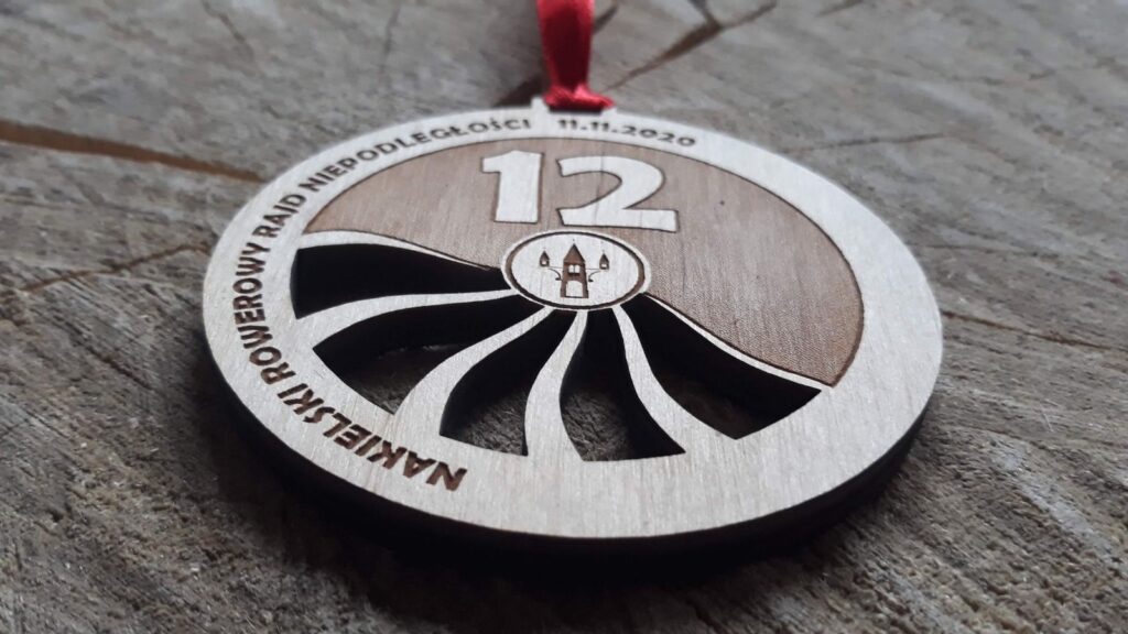 Okrągły drewniany medal na Rowerowy Rajd Niepodległości, ozdobiony ażurem imitującym szprychy rowerowe.