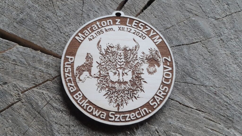 Okrągły medal ze sklejki o średnicy 8,5 cm i grubości 6 mm. Na gładkiej, jasnej powierzchni widnieje precyzyjny, głęboki grawer przedstawiający Leszego – mitologicznego opiekuna lasu. Medal zawieszony na jednobarwnej wstążce w leśnym odcieniu zieleni., lub sznurkierm. Tło neutralne, podkreślające naturalny charakter drewna.