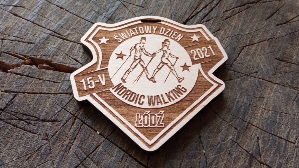 Drewniane medale w kształcie tarczy na Światowy Dzień Nordic Walking, z precyzyjnym grawerem przedstawiającym parę maszerującą z kijami oraz okolicznościowym napisem.