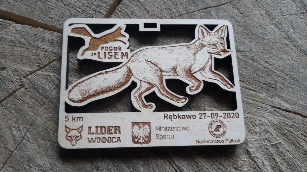 Prostokątny drewniany medal na bieg „Pogoń za lisem”, z precyzyjnie wyciętym ażurowym kształtem buta sportowego, grawerem uciekającego lisa oraz nazwą zawodów, wykonany z jasnej brzozy bez osmaleń.