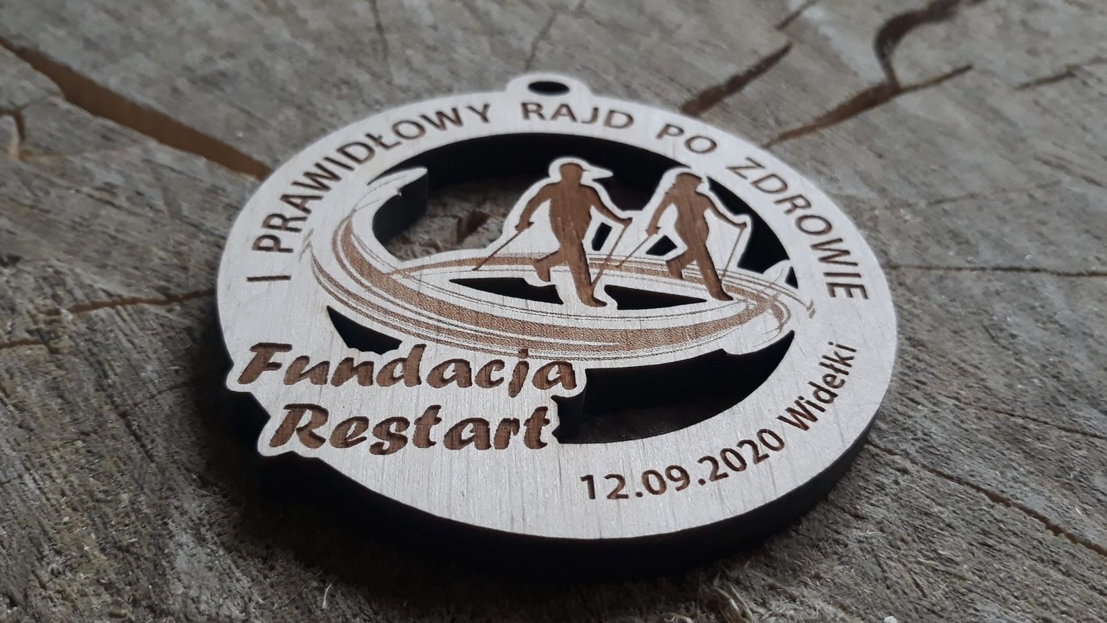 Okrągły drewniany medal na Rajd Po Zdrowie z ażurowo wyciętymi postaciami idącymi z kijkami. Nordic Walking.