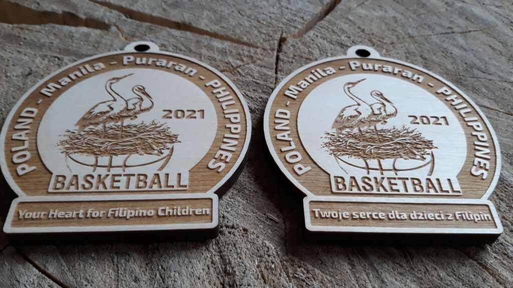 Okrągły drewniany medal o solidnej grubości 6 mm na akcję charytatywną „Basketball – Twoje serce dla dzieci z Filipin”, z grawerowanym gniazdem bociana, oraz nazwami lokalizacji: Poland, Manila, Puraran, Philippines.