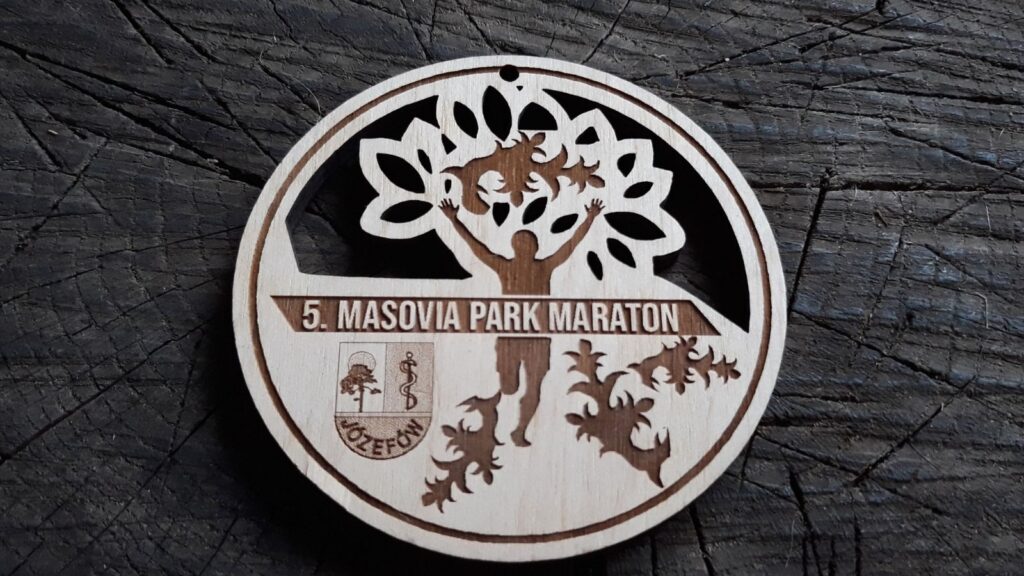 Ażurowy drewniany medal na „Masovia Park Maraton”, z precyzyjnie ażurowo wyciętymi motywami liści dębu, sylwetką biegacza z rękami w górze oraz herbem, wykonany z czystej płyty brzozy bez śladów dymu i osmaleń.