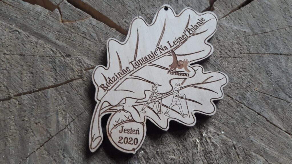Ekologiczny drewniany medal w kształcie liścia dębu z grawerowaną szyszką, przygotowany na wydarzenie Rodzinne Tuptanie.