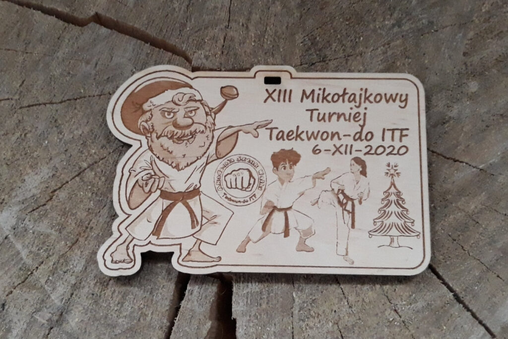 Drewniany medal na mikołajkowy turniej Taekwon-do z grawerem Świętego Mikołaja w stroju do sztuk walki wykonującego kopnięcie, araz grawerem młodych adeptów taekwon-do, choinki, loga i napisów