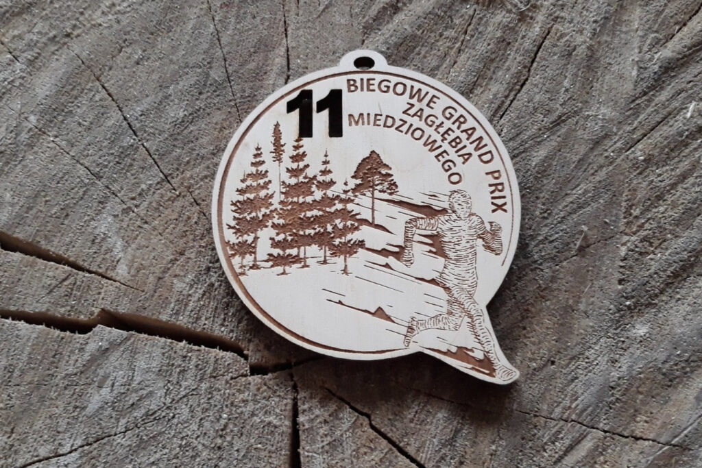 Okrągły drewniany medal na Biegowe Grand Prix z dynamicznym grawerem pędzącego biegacza i ozdobnym motywem sportowym.
