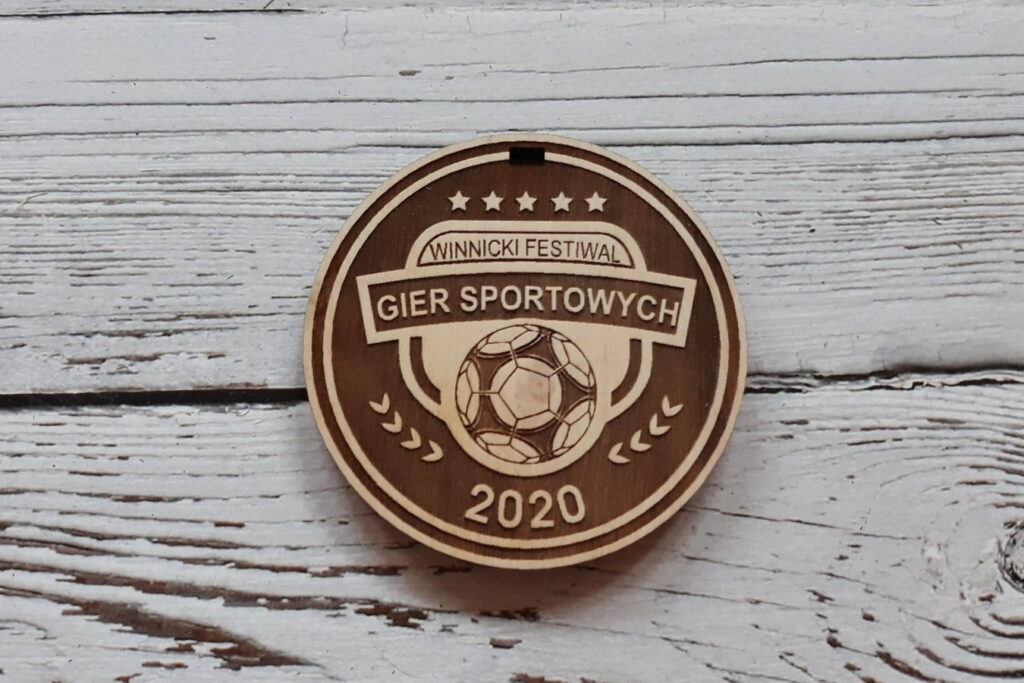 Klasyczne okrągłe drewniane medale na Festiwal Gier Sportowych z precyzyjnym grawerem nazwy wydarzenia, roku oraz grafiką symbolizującą sportową rywalizację.
