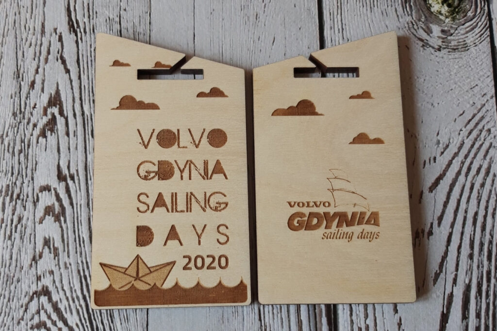 Dwustronnie grawerowany drewniany medal na regaty „Sailing Days”, przedstawiający żaglówkę na falach z jednej strony oraz szczegółowe informacje o wydarzeniu z drugiej.