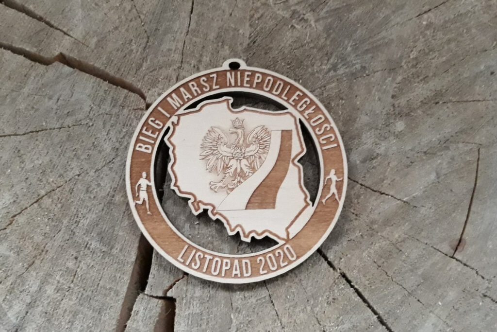 Okrągły ażurowy medal drewniany na Bieg i Marsz Niepodległości z wyciętym symbolem orła białego, flagą, konturem Polski oraz datą 11 listopada.