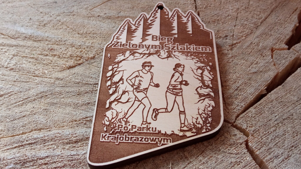 Ekologiczny drewniany medal o solidnej grubości 6 mm na edycję zawodów „Bieg Zielonym Szlakiem po Parku Krajobrazowym”, z precyzyjnym grawerem krętej ścieżki w sercu gęstego lasu, na ścieżce biegacz, w oddali zarys drzew.