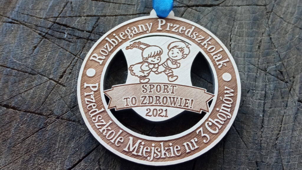 Okrągły drewniany medal dla dzieci z grawerowaną uśmiechniętą sylwetką biegnących przedszkolaków, na środku napis Sport to Zdrowie.