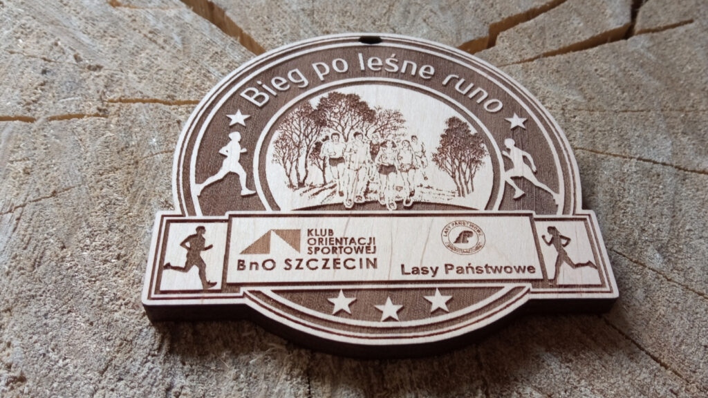 Ekologiczny drewniany medal o solidnej grubości 6 mm na „Bieg o Leśne Runo”, z precyzyjnym grawerem bogatego poszycia leśnego, drzew, ścieżki leśnej, oraz dynamicznych sylwetek biegaczy trailowych.