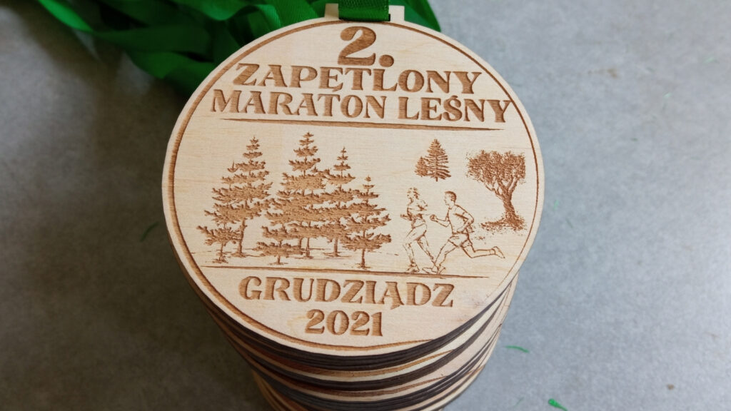 Okrągły drewniany medal o solidnej grubości 6 mm na „2. Zapętlony Maraton Leśny” z precyzyjnym grawerem biegaczy na skraju lasu.