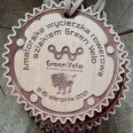 Okrągły ekologiczny drewniany medal o solidnej grubości 6 mm na „Amatorską Wycieczkę Rowerową Szlakiem Green Velo”, z precyzyjnym grawerem żubra, charakterystyczną ramką w kształcie blatu korby rowerowej, powieszony na rzemieniu.