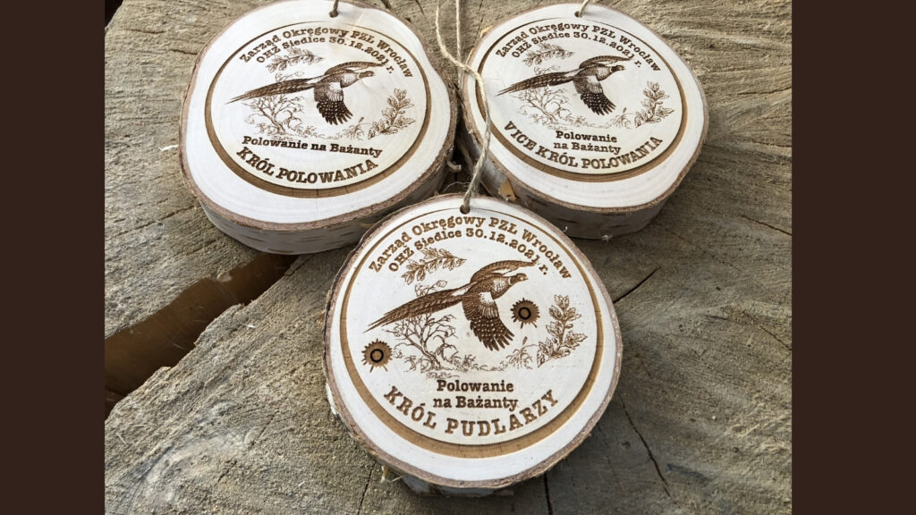 Drewniany medal na plastrze drewna (brzozy) z naturalną korą dla „Króla Pudlarza” z okazji polowania na bażanty, z grawerowaną sylwetką bażanta zrywającego się do lotu oraz okolicznościowym napisem.