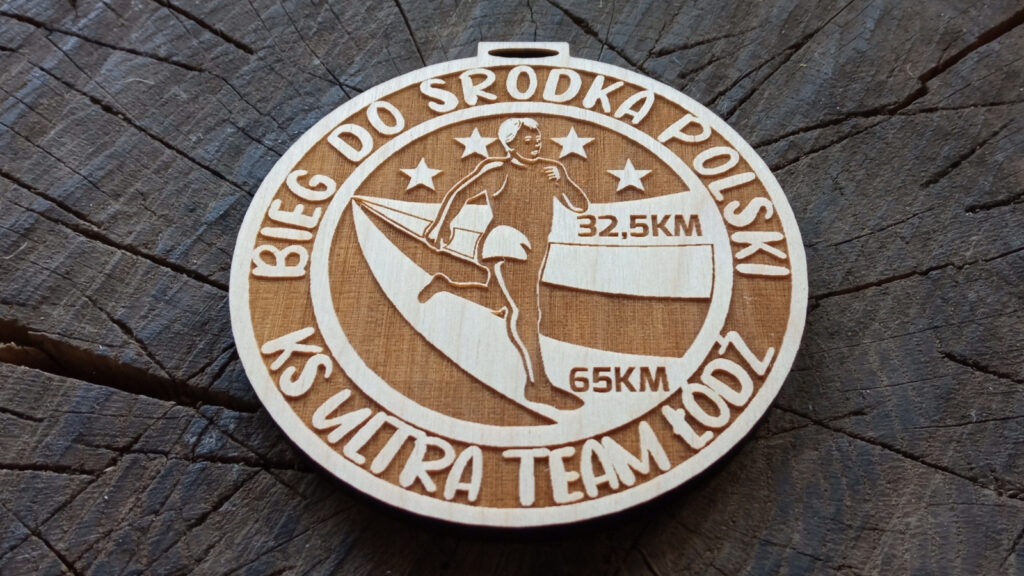 Okrągły drewniany medal o solidnej grubości 6 mm na „Bieg do Środka Polski”, z grawerowanym konturem mapy Polski, punktem oznaczającym środek kraju oraz sylwetką biegacza. Medal w ciekawej stylistyce obramowania.