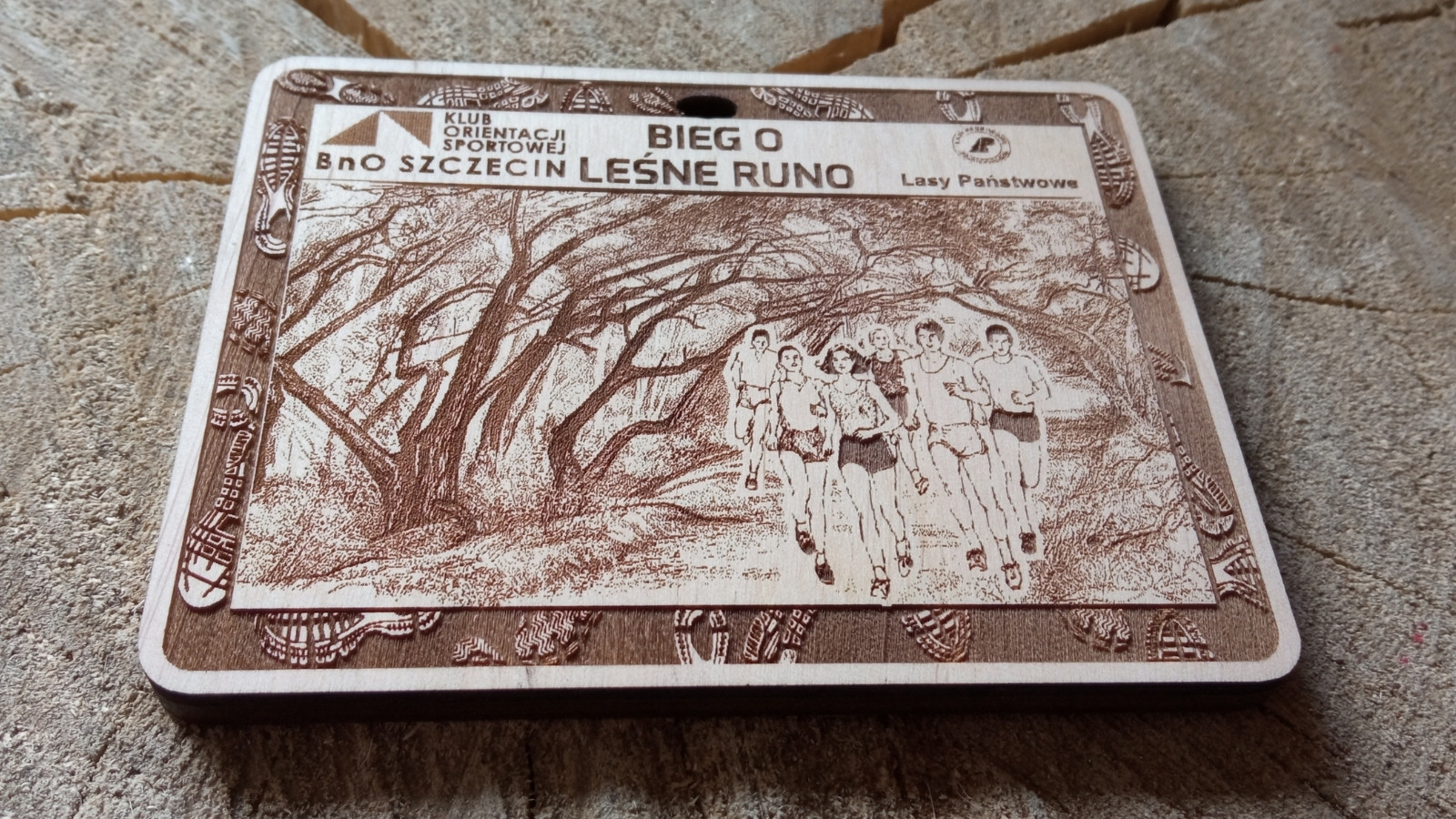 Ekologiczny drewniany medal o solidnej grubości 6 mm na „Bieg o Leśne Runo”, z precyzyjnym grawerem bogatego poszycia leśnego, drzew, ścieżki leśnej, oraz dynamicznych sylwetek biegaczy trailowych.