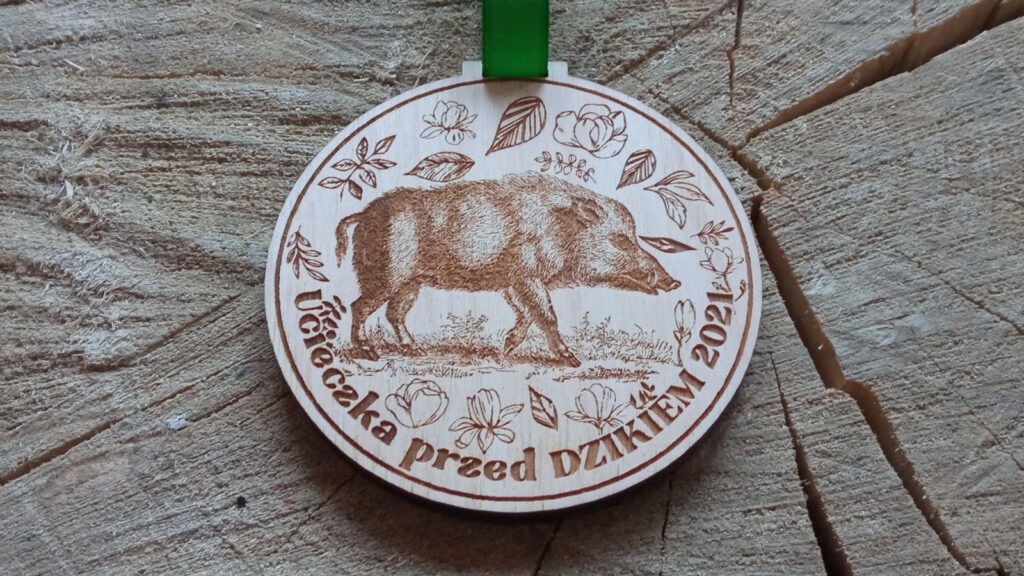 Okrągły drewniany medal o solidnej grubości 6 mm na zawody „Ucieczka przed dzikiem”, z dynamicznym grawerem szarżującego dzika, leśnymi motywami w tle oraz pamiątkową nazwą biegu.