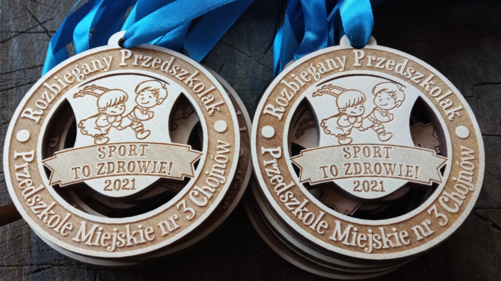 Okrągłe ażurowe drewniane medale o solidnej grubości 6 mm dla dzieci na event „Sport to zdrowie!”, z wyciętymi motywami sportowymi, gwiazdkami oraz radosnym grawerem hasła promującego zdrowy styl życia.