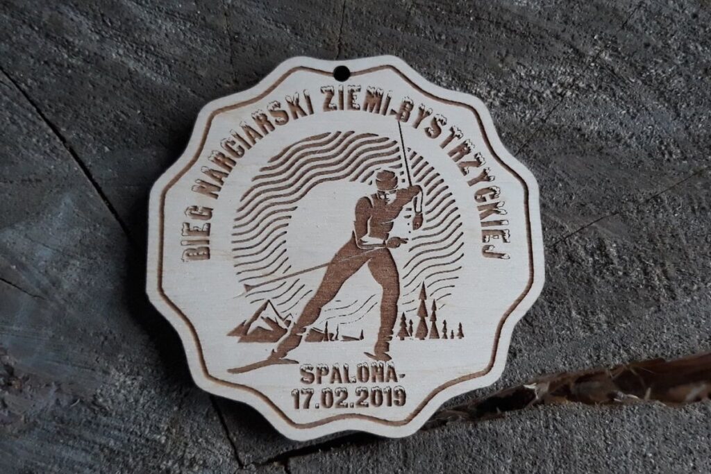 Drewniany medal pamiątkowy z Biegu Narciarskiego Ziemi Bystrzyckiej 2019 w Spalonej z grawerem narciarza.