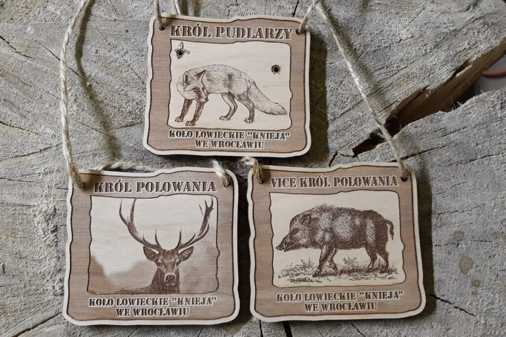 Zestaw trzech drewnianych medali łowieckich: Król Polowania z jeleniem, Vicekról z dzikiem oraz Król Pudlarzy z lisem, wykonane z grawerowanej sklejki z brzozy.