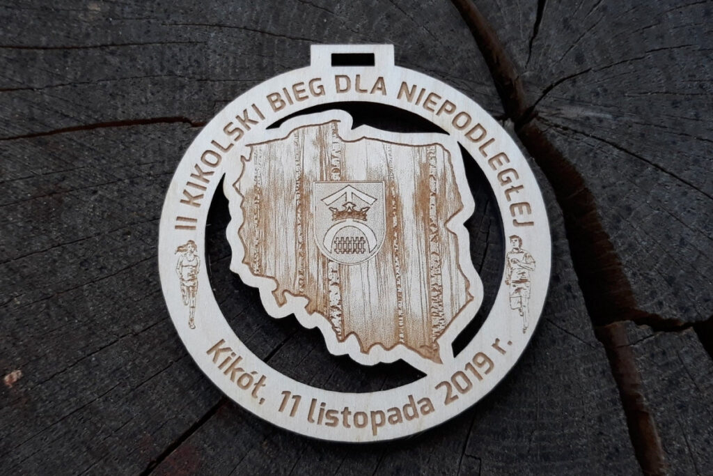 Okrągły drewniany medal z precyzyjnie wyciętym ażurowym konturem mapy Polski w środku, grawerowanym napisem Bieg dla Niepodległej i datą.