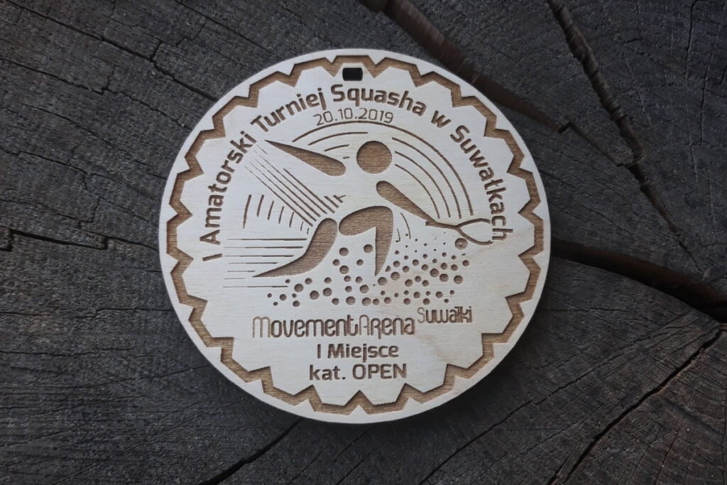 Okrągły drewniany medal do squasha z grawerem rakiety, charakterystycznej piłeczki z dwiema kropkami i gracza oraz napisami.