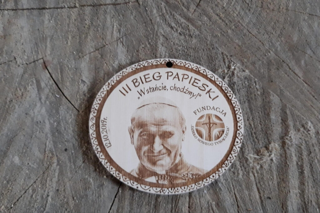 Owalny drewniany medal z realistycznym grawerem portretowym św. Jana Pawła II, napisem III Bieg Papieski i datą wydarzenia.