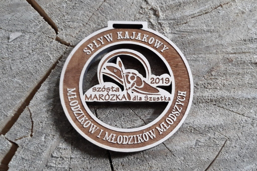 Okrągły drewniany medal z grawerem kajakarza na rzece, napisem Spływ Kajakowy Marózka oraz dedykacją dla ekipy Szustka.