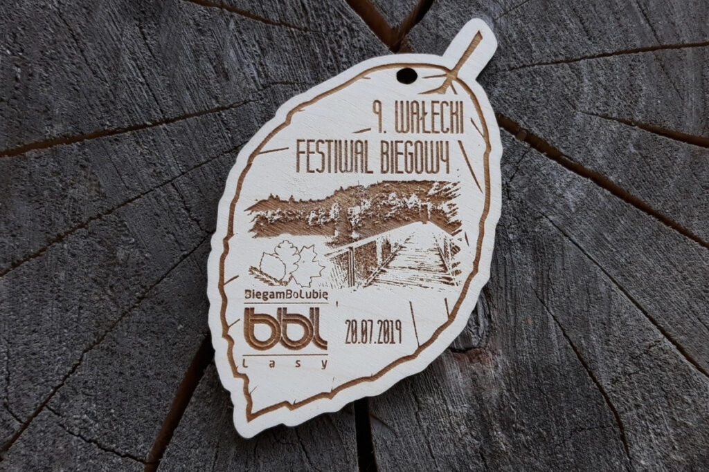 Drewniany medal wycięty w kształcie liścia dębu z grawerem logotypu Wałeckiego Festiwalu Biegowego.