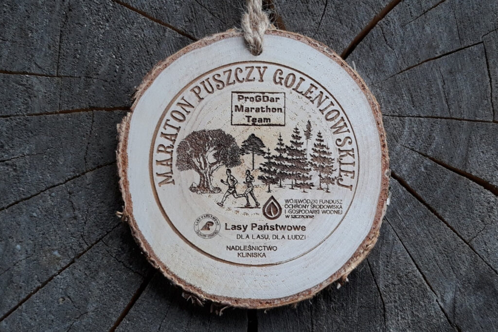 Medal z naturalnego plastra brzozy z korą, z grawerem panoramy lasu, biegacza oraz napisem Maraton Puszczy Goleniowskiej.