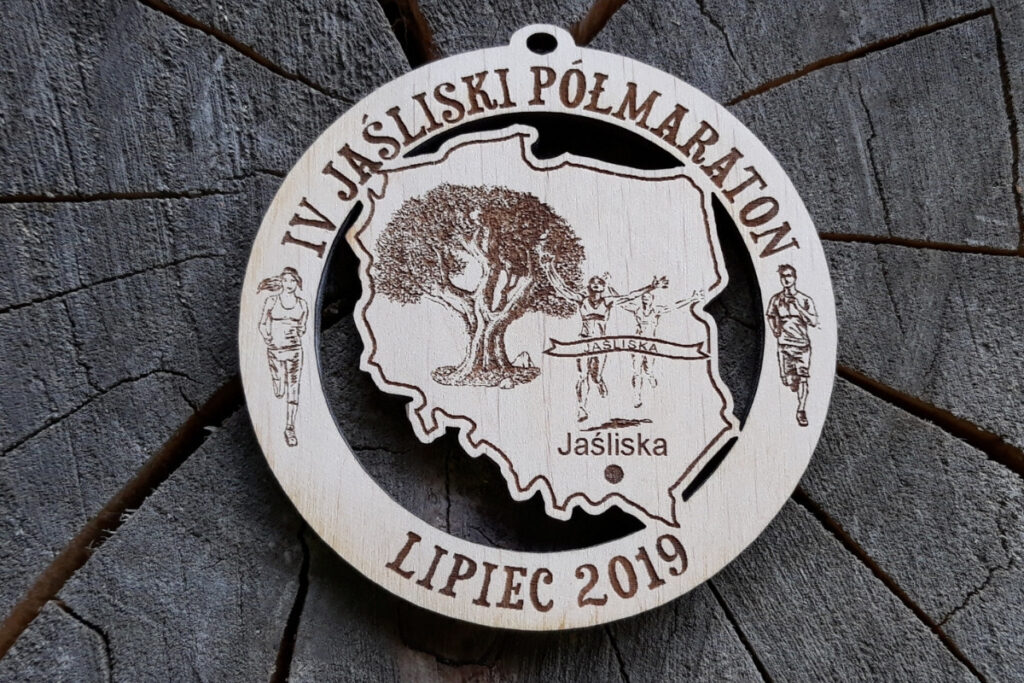 Okrągły drewniany medal z ażurowo wyciętym wewnątrz konturem Polski, grawerem IV Jaśliski Półmaraton oraz datą i lokalizacją biegu.