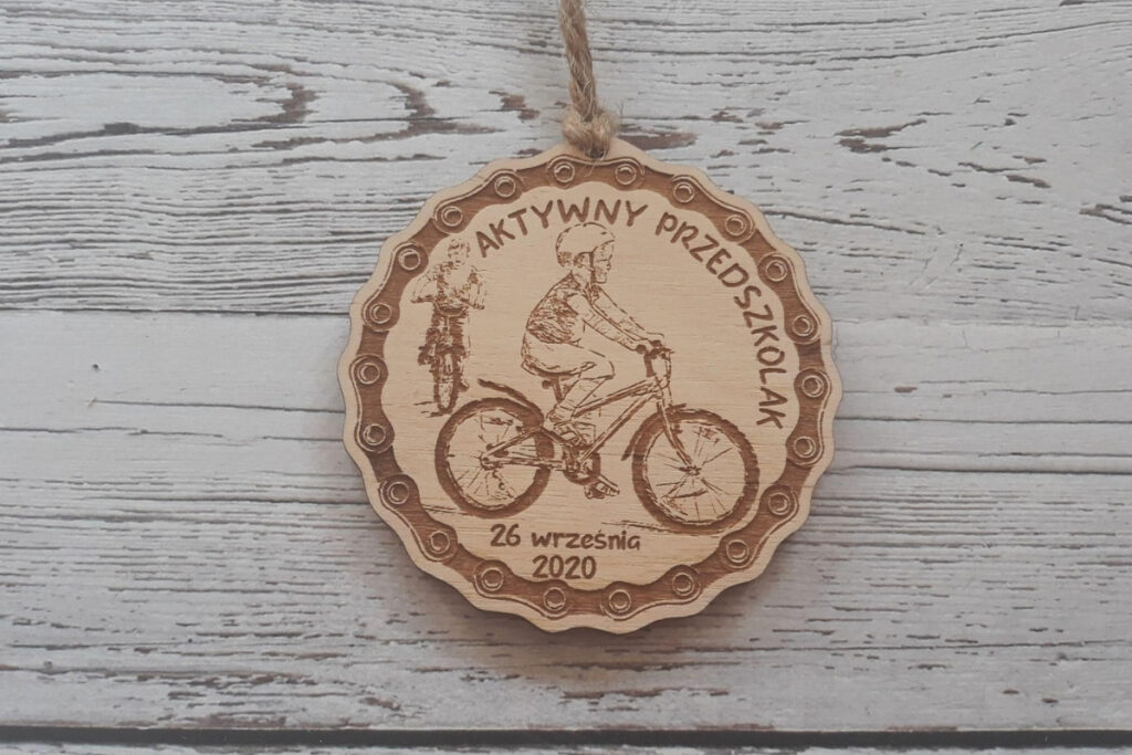 Okrągły drewniany medal dla dzieci z grawerem dziecka  w kasku na rowerze, napisem Aktywny Przedszkolak oraz datą.