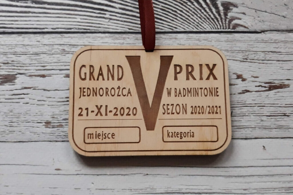 Drewniany medal na V Grand Prix Jednorożca w Badmintonie z grawerem lotki, logotypem wydarzenia oraz specjalnym miejscem na wpisanie zajętego miejsca i kategorii, czyste wykończenie bez osmaleń.