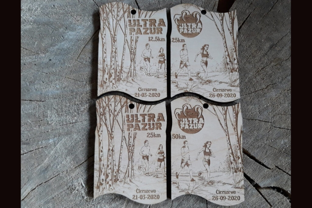 Zestaw dwóch drewnianych medali modułowych na bieg Ultra Pazur, które po złączeniu tworzą prostokątną tabliczkę z motywem drapieżnych pazurów i logotypem biegu, wykonany z czystej brzozy bez śladów dymu.